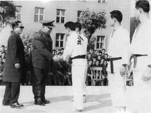 Ein Offizier in Uniform begrüßt Männer im Dobok vor einem Gebäude