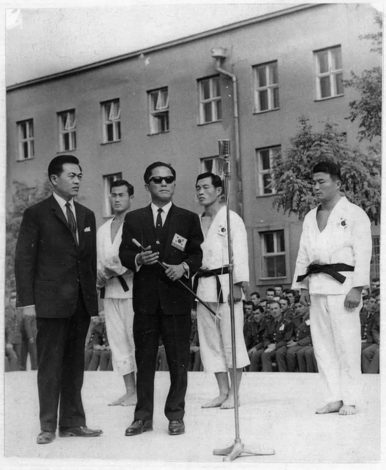 Choi Hong-Hi im Anzug neben einem Offiziellen und vier Männern im Dobok vor einem Gebäude