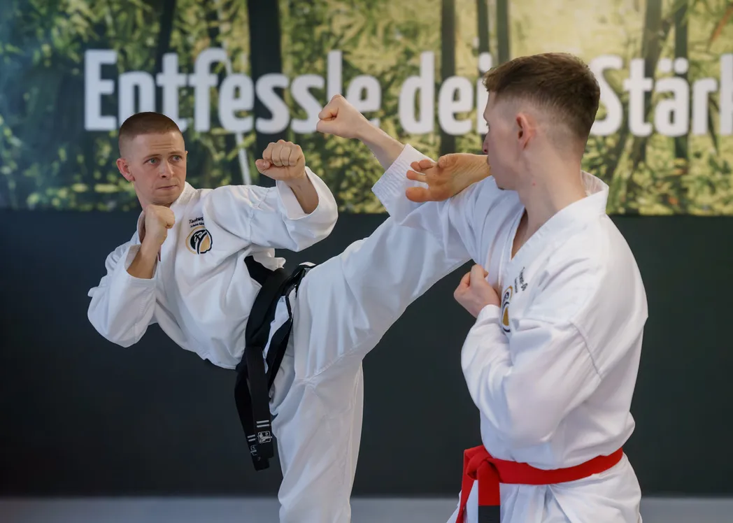 Zwei erwachsene Taekwon-Do-Trainierende bei einer kontrollierten Partnertechnik, ein Kick wird knapp vor dem Trainingspartner gestoppt