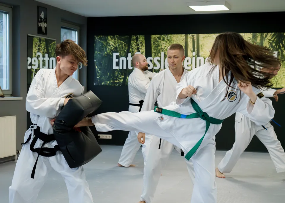Jugendliche mit grünem Gurt führt einen kontrollierten Kick gegen ein Pratzenpolster aus, im Hintergrund weitere Trainierende der Taekwon-Do Schulen Könnecke