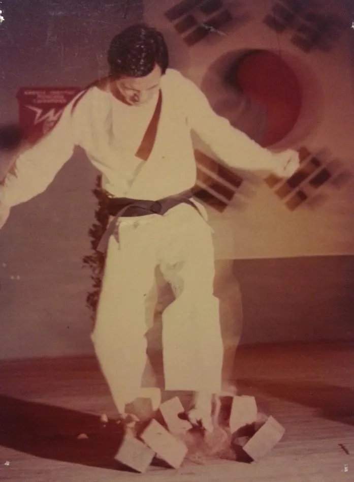 Kwon Jae-Hwa im Dobok über zerbrochenen Steinen auf einer Bühne vor koreanischer Flagge