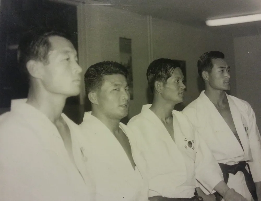 Vier Männer im Dobok mit koreanischen Flaggenabzeichen stehen im Profil nebeneinander